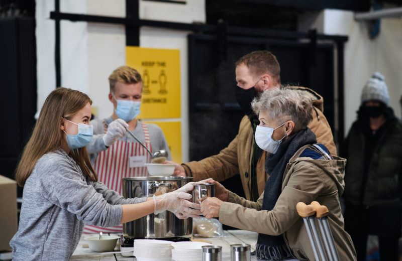 Volunteers serving hot soup for ill and homeless in community charity donation center, food bank and coronavirus concept.